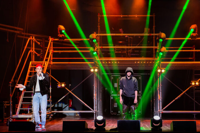 Cirano deve morire - una scena dello spettacolo con tre ragazzi vestiti da rapper e tanti fasci di luce intorno a loro illuminano il palco