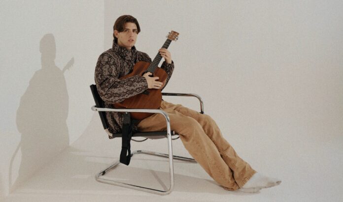 primogenito seduto su una sedia di metallo, imbraccia una chitarra acustica