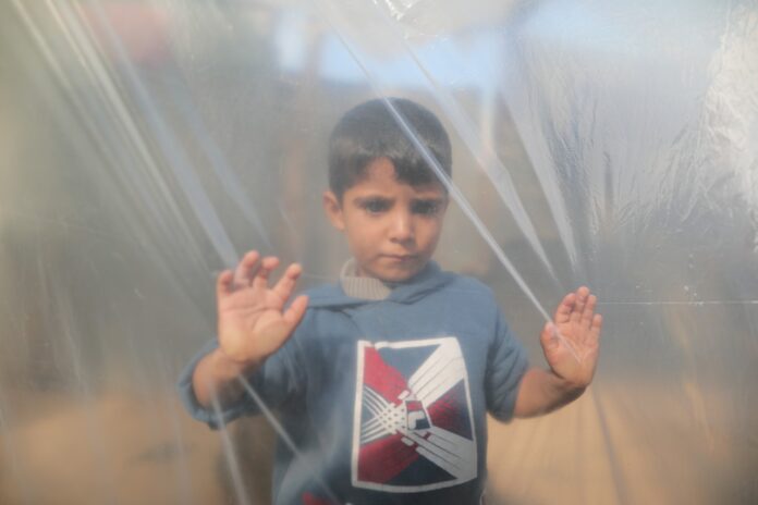 Guerra di Gaza - un bambino con maglietta azzura è in un campo e d è appoggiato ad un telone di nailonche rende sfocata la foto