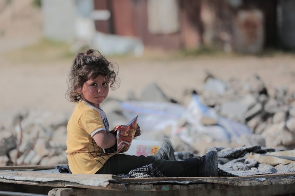 Una bambina in mezzo alle macerie della guerra ha la mano dentro una busta probabilmente di qualcosa da mangiare. 