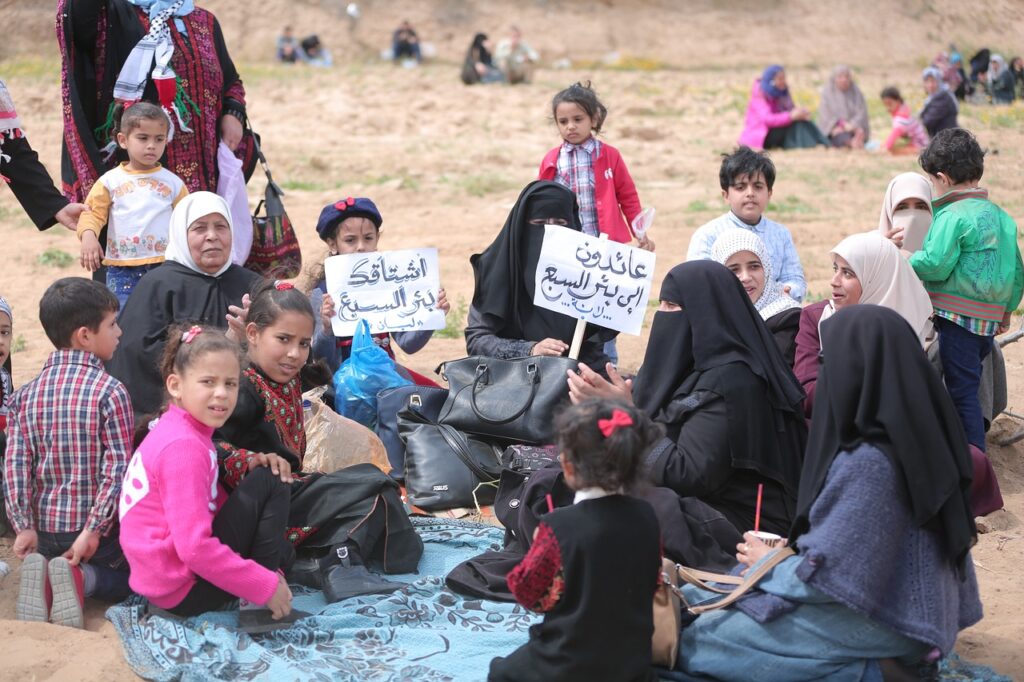 Guerra di Gaza, un gruppo di donne e bambini sono seduti in cerchio. Le donne indossano il burka , i bamibni tengono in mano dei cartelli con scritte in arabo