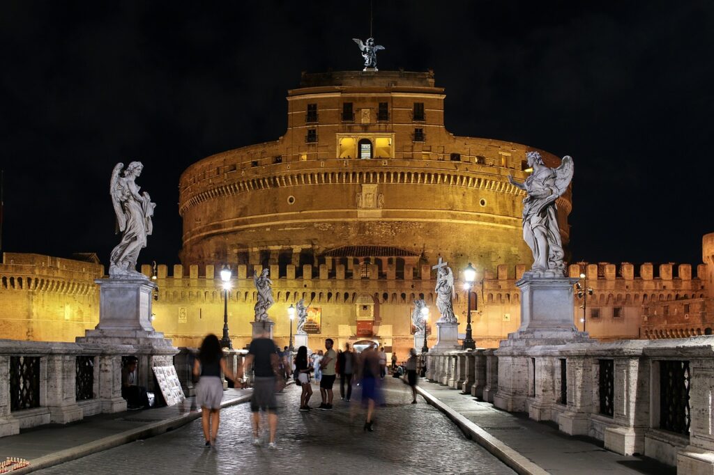 Castel sant'Angelo a Roma - vista notturna dal ponte con tante statue. Il castello è rotondo sovrastato da una torre sormontata dalla  statua di un angelo