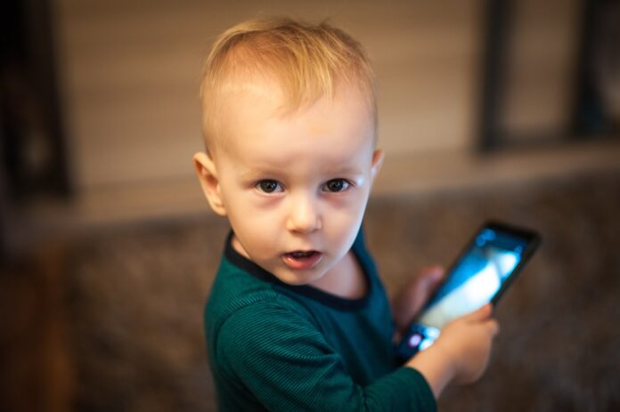 bambini su internet explicit contents - un bimbo guarda verso l'obbiettivo e tiene in mano un cellulare