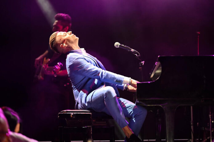 Matthew Lee seduto al pianofortee, indossa un vestito azzurro, durante un concerto
