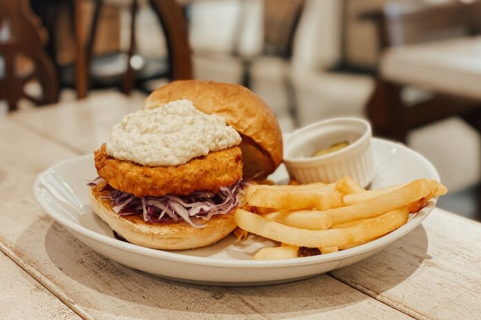 Veganismo - un hamburger vegano con verdure, affianco delle patatine fritte e uno scodellino di salsa, il tutto in un piatto bianco