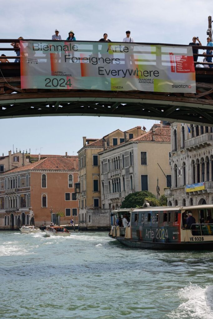 uno striscione della biennale su un ponte di Venezia con un vaporetto che passa sotto