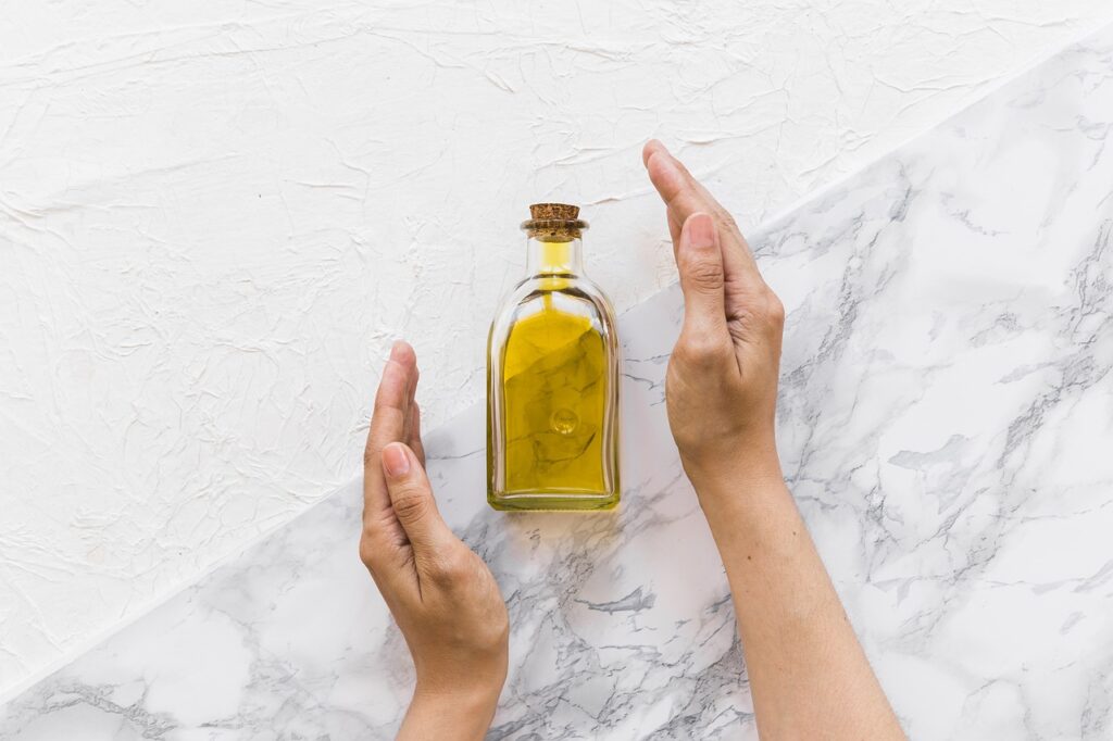 Olio Evo -una bottiglia posata su un marmo bianco e due mani aperte in segno di protezione