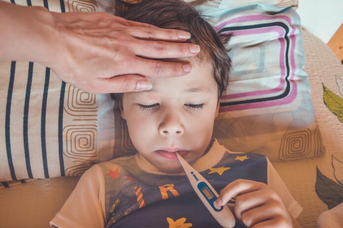 streptococco - un bambino è sdraiato nel letto con un termometro in bocca, ha l'aria sofferente e la mamma gli sta toccando la fronte