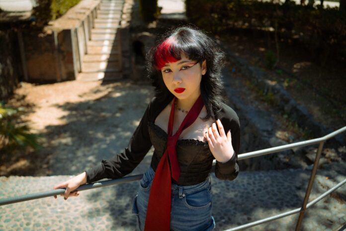 roberta scandurra in primo piani, indossa jeans, camicia nera, cravatta granata, ha i capelli neri lunghi con una ciocca rossa