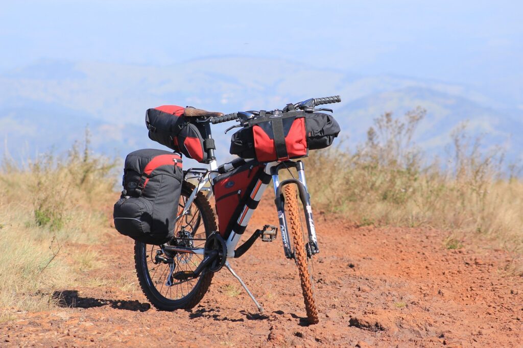 cicloturismo - una bicicletta appoggiata sulsuo cavalletto in mezzo a un sentiero di montagna, con diverse sacche e szain attaccati