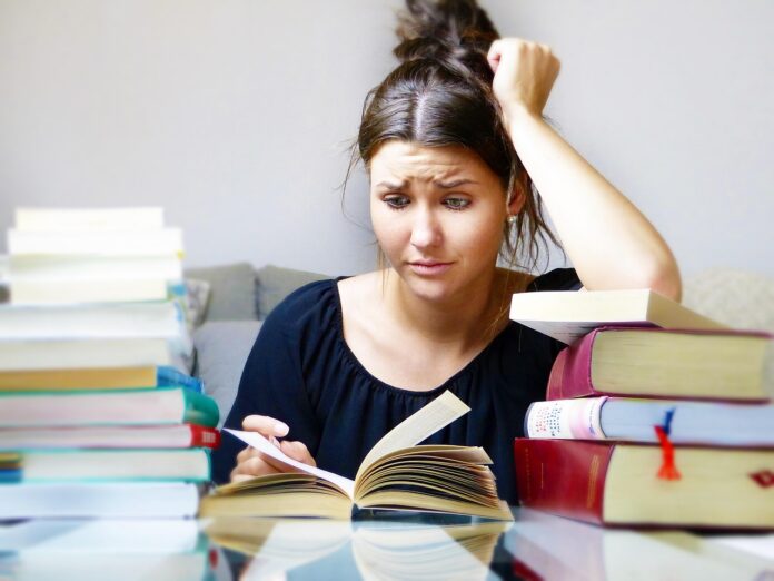 Motte prima degli esami maturità - una ragazza ha l'aria preoccupata davanti a un apila di libri. Sta leggendo su un libro, ha i capelli neri raccolti sulla testa e ha la testa appoggiata alla mano