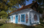 casa con parti bianche e porte azzurre incorniciate di ghirlande colorte di fiori a zalipie