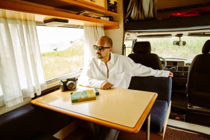cortese seduto all'interno di un camper, indossa una camicia bianca