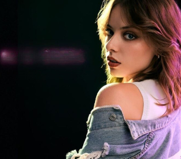 serena viel di profilo, idossa una canotta bianca e un giubboto di jeans che le lascia scoperta una spalla