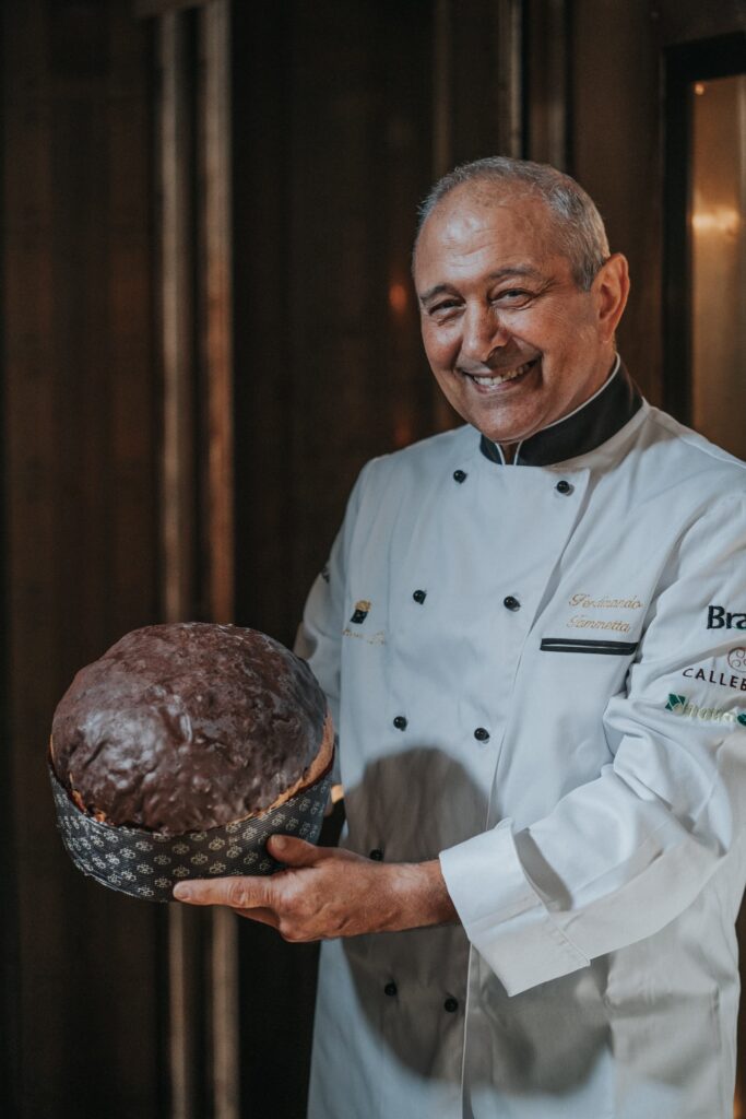 panettone al cioccolato in mano a un uomo vestito con divisa bianca da pasticcere