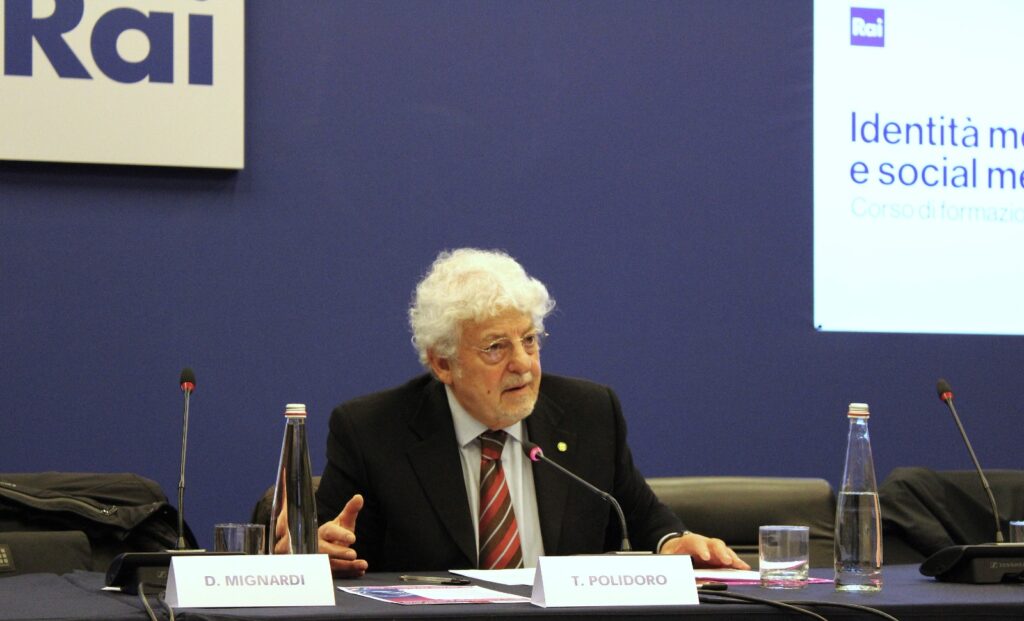 Tommaso Polidoro corsi di formazione per giornalisti - nella foto, Tommaso Polidoro con capelli ricci bianchi sta parlando seduto a un tavolo conferenze, Indossa giacca scusa, camicia bianca, cravatta rossa e occhiali