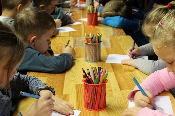 asilo gratuito bambini disabili - un tavolo con intorno dei bimbi che disegnano e in mezzo al tavolo giallo dei portamatite con tante matite colorate
