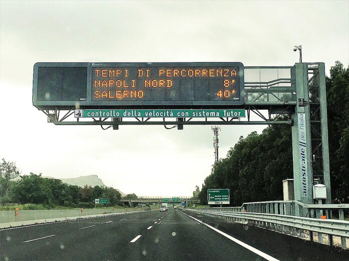 Tutor 3.0 dove sono e come funzionano Attenzione nuove multe - Zetatielle Magazine - un'autostrada con un ponte in ferro che la sovrasta con pannelli stradali che indicano ln arancione la scritta 