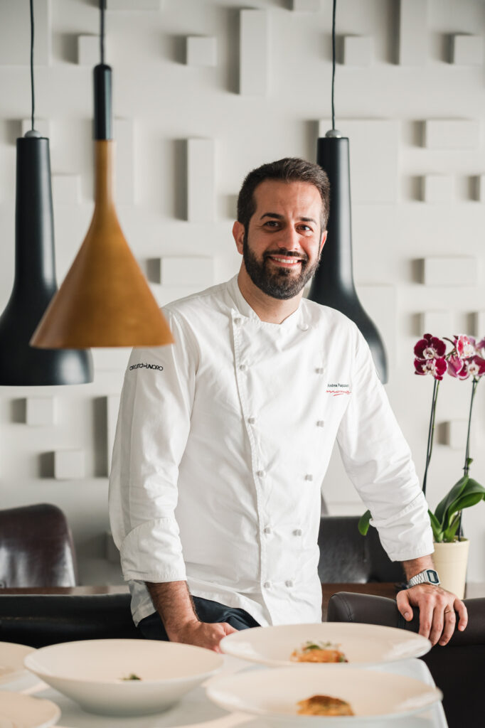 Un uomo con divisa da chef sorride guardando l'obbiettivo
