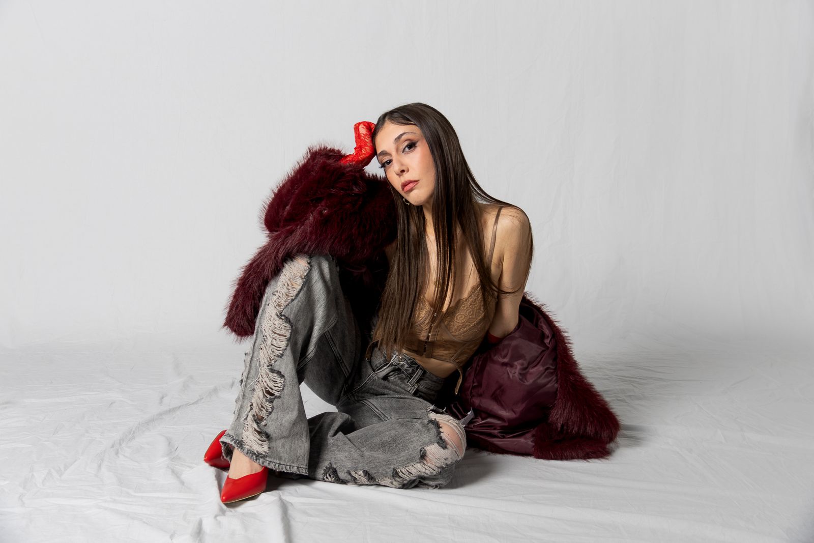 chiodi - zuia in primo piano indossa jeans con gli strappi e una pelliccia rosso scuro