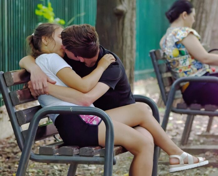 Delitto Afragola genitori - nella foto due ragazzini che si baciano su una panchina, a ffianco, su un'altra panchina una signora con camicia a fiori volta la schiena ai ragazzi e legge