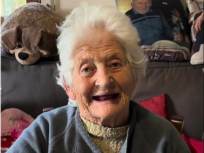 Nonna Luigina tiktok influencer social - nella foto una signora molto anziana con occhi azzurri capelli bianchi senmza denti sorride. E' seduta su un divano e indossa un maglioncino azzurro