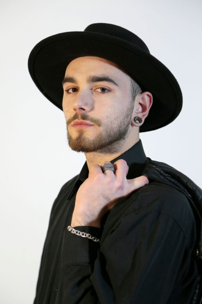 emmecappa in primo piano, indossa camicia e cappello scuri