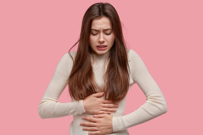 Nutraceutica incintinenza - sfondo rosa, una donna a mezzo busto, capelli lunghi maglia bianca attillata, ha le due mani sulla pancia e ha una smorfia di dolore