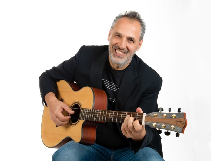 Conversazioni-musicali-con l'IA - Reno-Brandoni in primo piano imbraccia una chitarra acustica