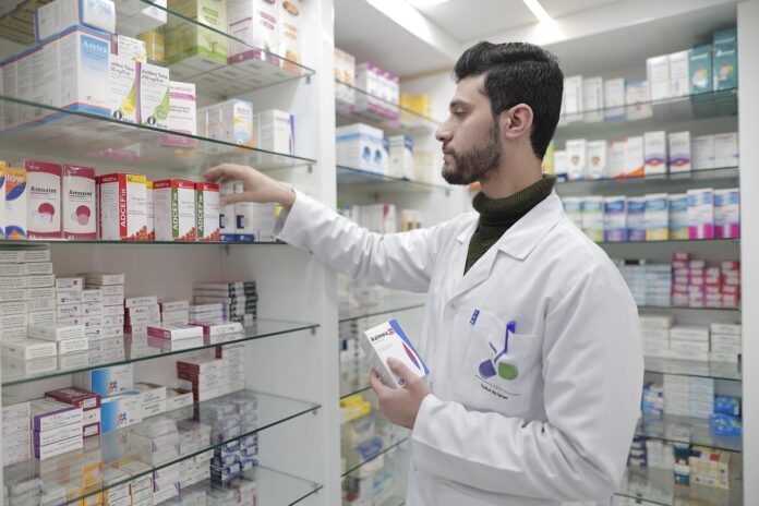 Farmacia e prevenzione - nella foto un medico con camice bianco sta mettendo a posto dei farmaci su uno scaffale della farmacia