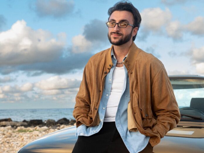 Keevuitton appoggiato al cofano di una macchina, indossa camicia e giubbotto di renna beige