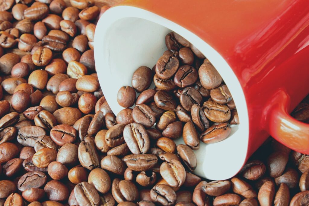 Perchè il caffè costa più caro - nella foto una tazzina rossa rovescia dei chicchi di caffè su un mucchio di chicchi