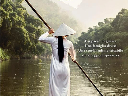 Quando le montagne cantano - Una donna vietnamita di schiena con cappello a cono abito bianco lungo sta remando con un remo molto lungosu una piroga che va su un fiume costeggiato da alberi