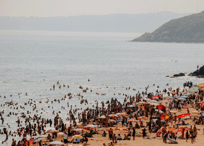 Ferragosto cosa lega le code in autostrada all’antica Roma - nella foto una veduta di una spiaggia gremita di persone in costume da bagno e tanta gente in mare che fa il bagno, sullo sfondo un pormontorio