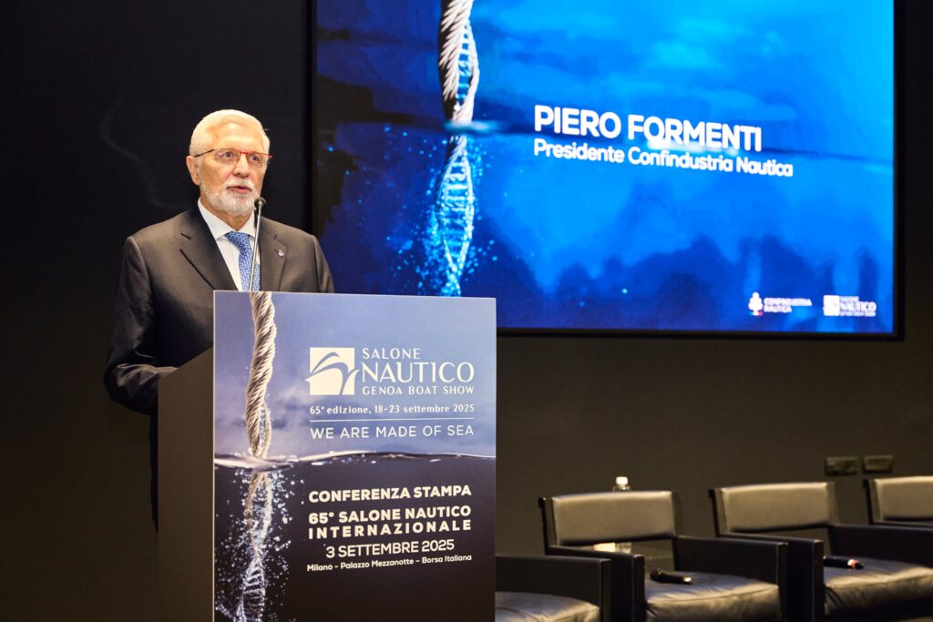 Salone nautico Genova - un uomo con barba e capelli bianchi, indossa occhiali, vestito con giacca scura cravatta azzurra, sta parlando allo scranno , dietro di lui un led wall con il nome Piero Formenti