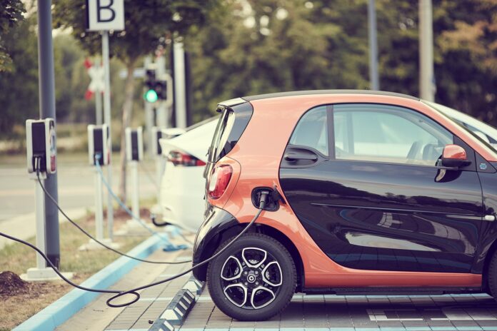 Incentivi auto elettriche - nella foto un auto elettrica bicolore nero e ruggine è attaccata con il filo alla colonnina di ricarica