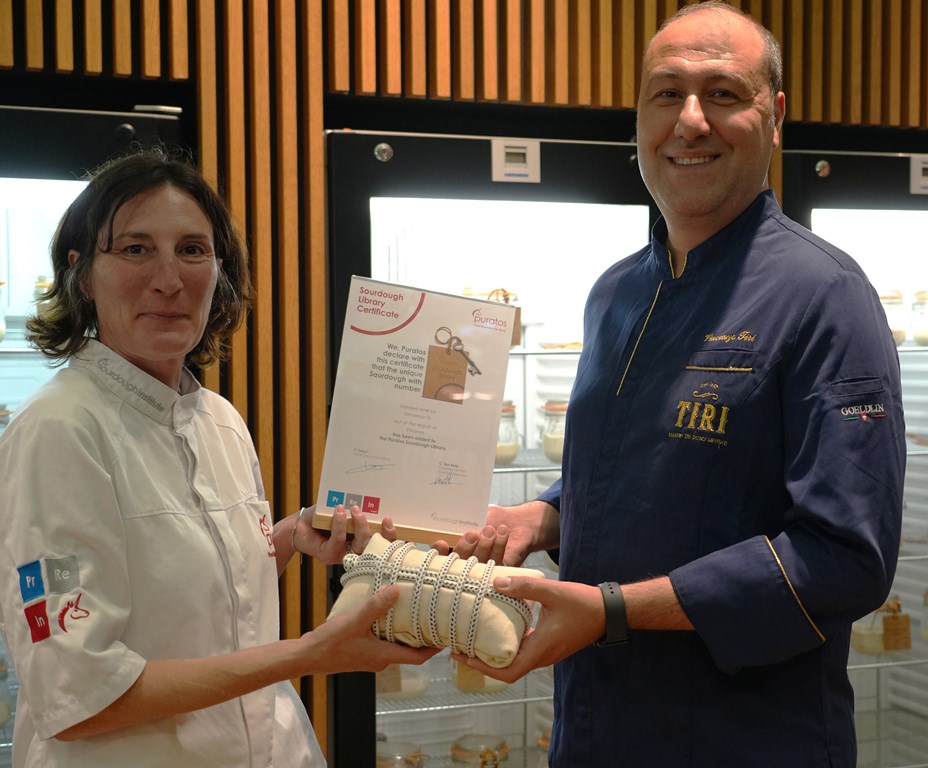 Biblioteca del Lievito Madre - nella foto una signora con camice bianco da pasticcere consegna un fagotto e una targa ad un uomo . Entrambi sorridono