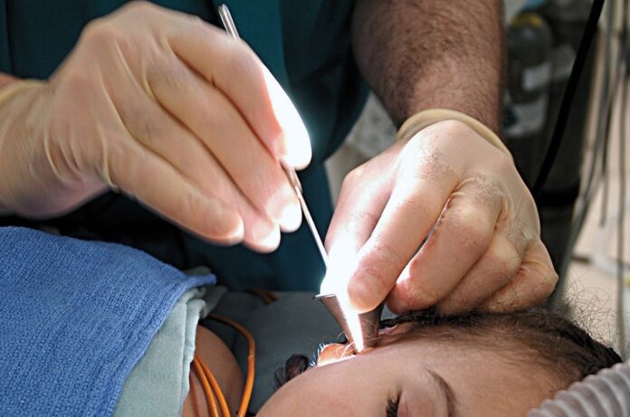 Melanoma - due mani con guanti in lattice appartengono a un chirurgo che sta effettuando un'operazione con penna laser sul viso di una donna che sta dormendo
