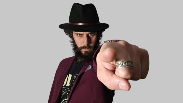 ramo - hawaii - il cantautore in primo piano, indossa giacca rosso scuro e cappello nero e ha il dito indice della manosinistra punato verso l'obiettivo