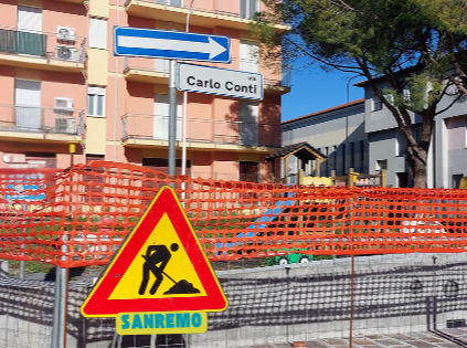 Sanremo è a Sanremo cronaca di una bufala annunciata - un cantiere crecintato con rete rossa, un cartello triangolare con l'omino dei lavori in corso e sotto la scritta Sanremo, il palo indicatore di una via con la scritta Via Carlo Conti e dietro dei palazzi