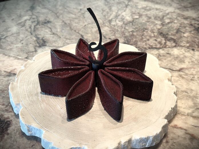 Belcolade Award 2025 - una torta bianca con sopra delle foorme romboidi di cioccolato disposte in modo da formare i petali di un fiore