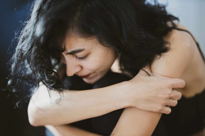 Giornata mondiale della salute mentale e Telefono Amico Italia - nella foto una donna in primo piano con capelli lunghi neri è seduta per terra, abbraccia le ginocchia
