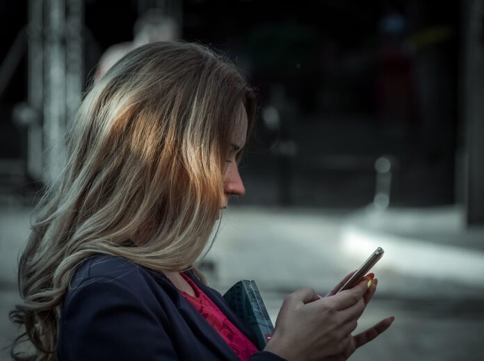 spoofing telefonico - una donna di profilo, con lunghi capelli biondi sta guardando il cellulare con aria incuriosita