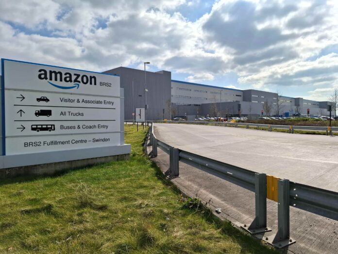 Tagli al personale in casa Amazon arriva l'IA - Zetatielle Magazine - BRS2_Amazon_fulfilment_centre_in_Swindon_2025_01 (1) Tagli al personale in Amazon, nella foto le palazzine degli uffici commericali dell azienda, sulla destra le indicaizoni per gli uffici in un pannello piantato in un prato verde davanti a una strada