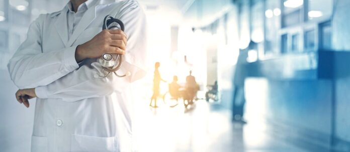 medici chirirghi - nella foto in primo piano il mezzo busto di un medico con in mano uno stetoscopio e sullo sfondo sfocato delle persone in arancione