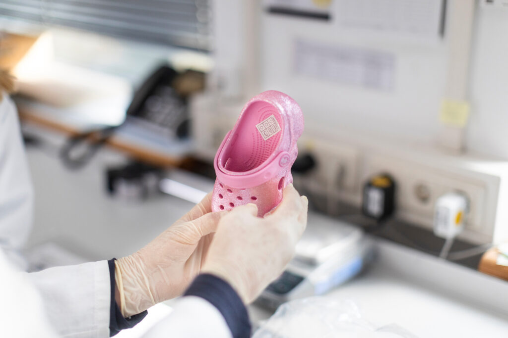 Fast Fashion - due mani da uomo che indossa un camice bianco tengono stretta una ciabattina rosa da bambina