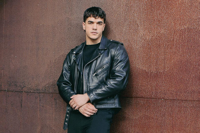 manuel dang in primo piano, appoggiato a un muro, indossa un giubbotto di pelle nera