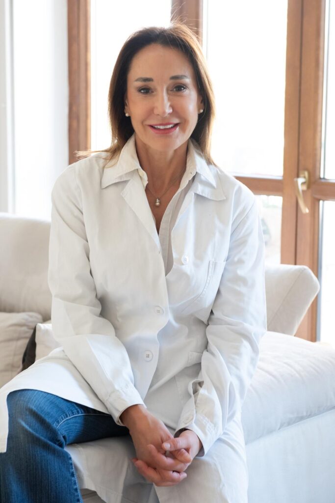 Medicina Estetica Rigenerativa - nella foto la dott.ssa Muraglia indossa un camice bianco, jeans, ha lunghi capelli neri e sorride seduta su un divano