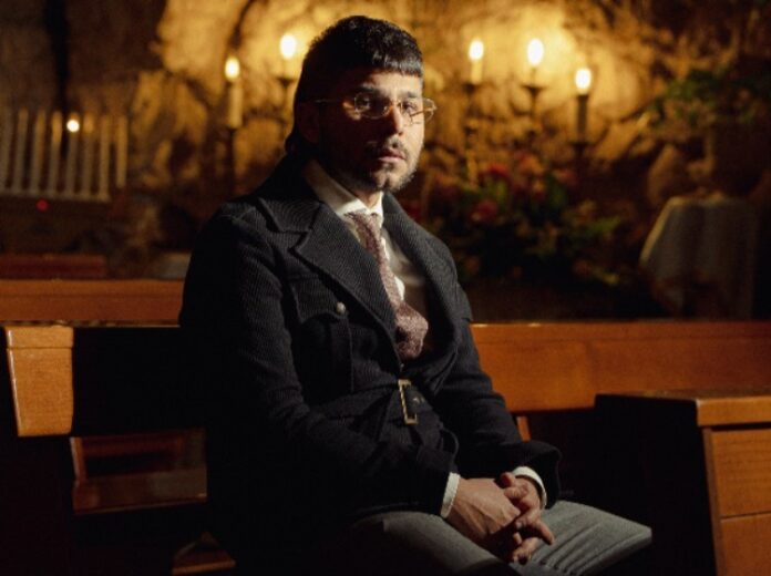 Padre Nostro la rivisitazione urban di Double G - etatielle Magazine - DOUBLE G_Foto padre nostro - double g in primo piano, vestito di scuro, seduto su una panca in chiesa