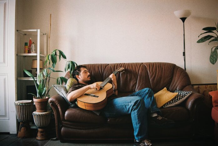 roberto montisano sdraiato su un divno, intento a suonare la chitarra